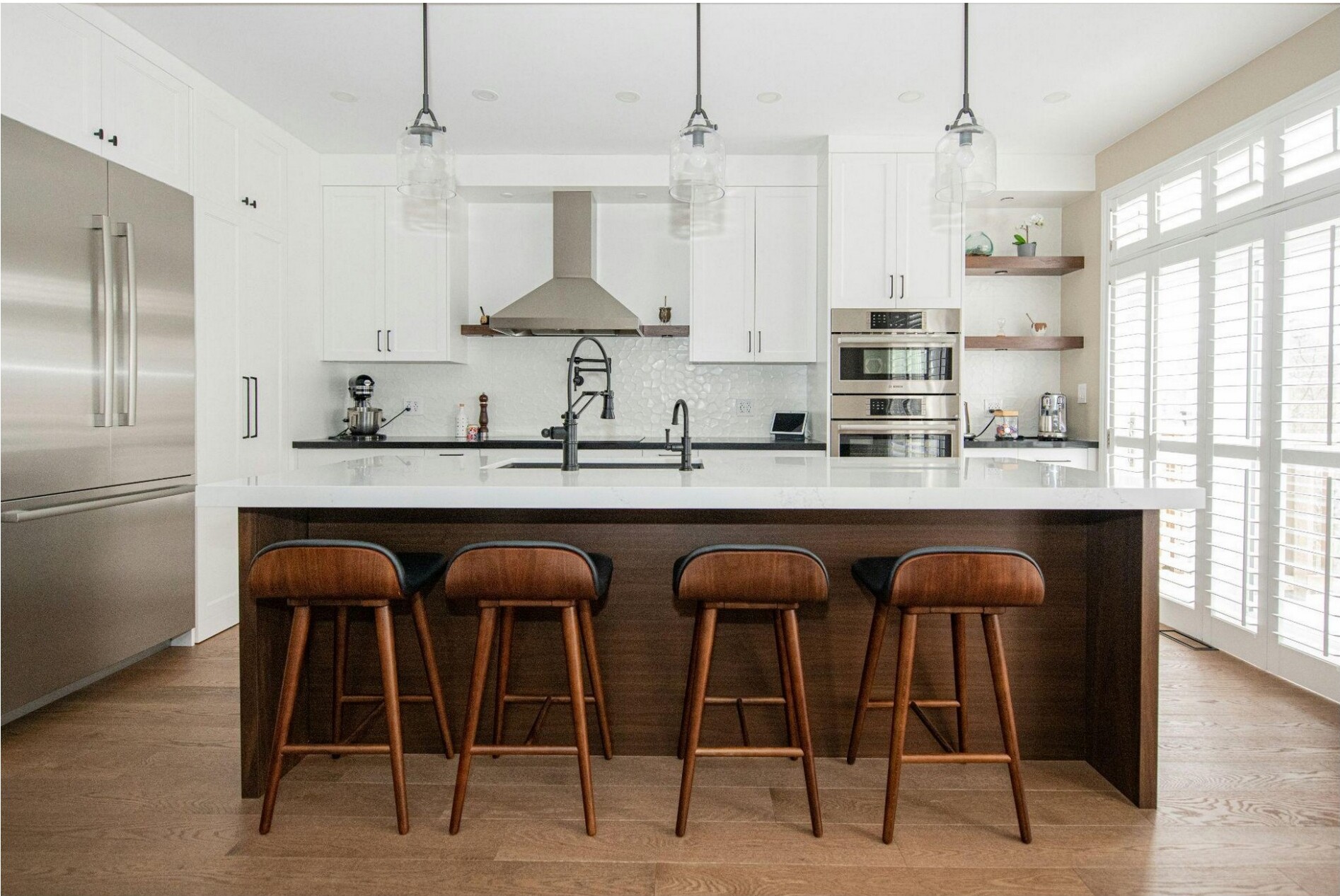A modern kitchen with white cabinets, stainless steel appliances, and wooden bar stools