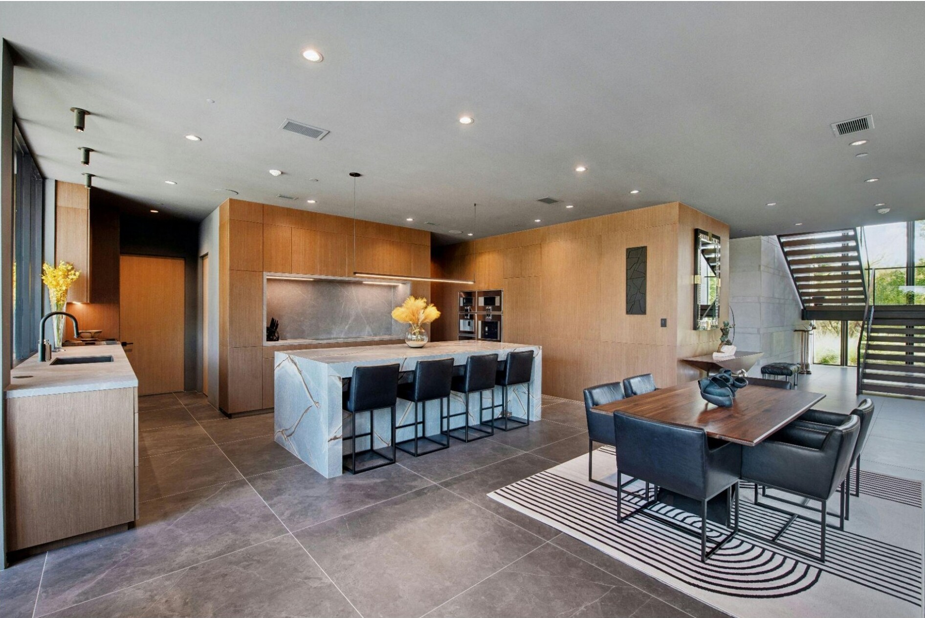 Modern kitchen and dining area with wood cabinetry, marble island, and large windows